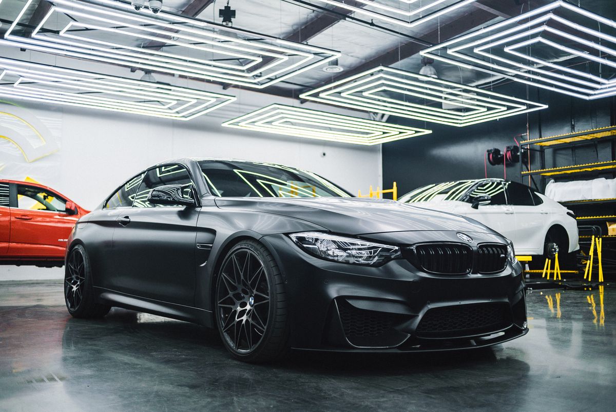 A matte-black BMW M4 with clean wheels parked in a detailing studio.