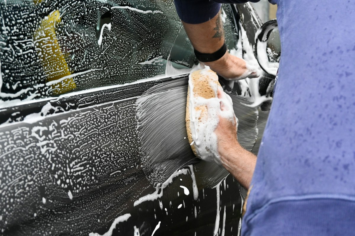 Close-up of a detailer hand-washing a car door panel with a sponge and soap suds, the kind of hands-on process a legitimate detailer should be able to describe clearly before you book