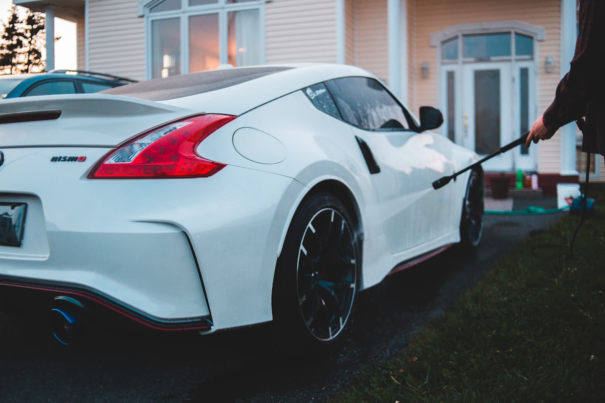 A clean white sports car being rinsed in a driveway at golden hour after a hand wash