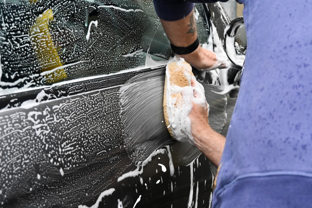 Hand washing a car with sponge and soap — the kind of maintenance visit a detailing membership provides