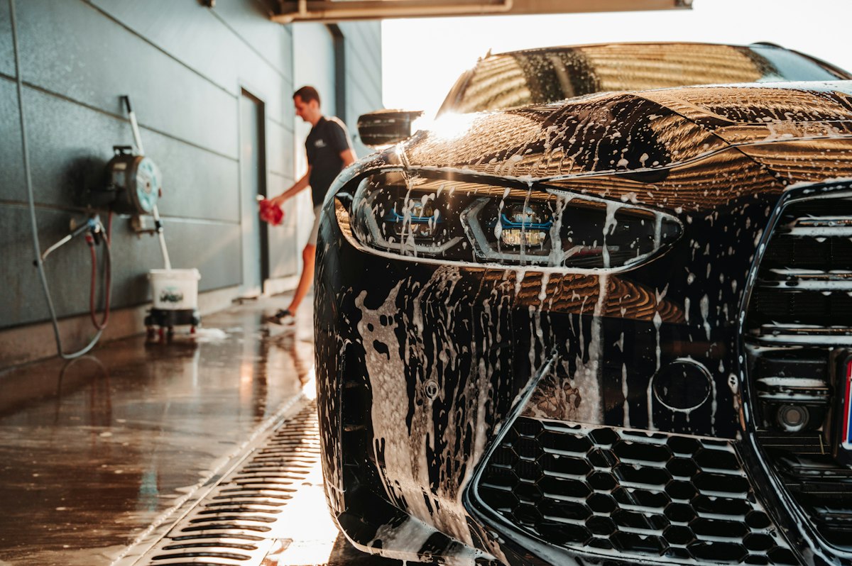 A detailer hand washing a car with soap suds in a covered detailing bay