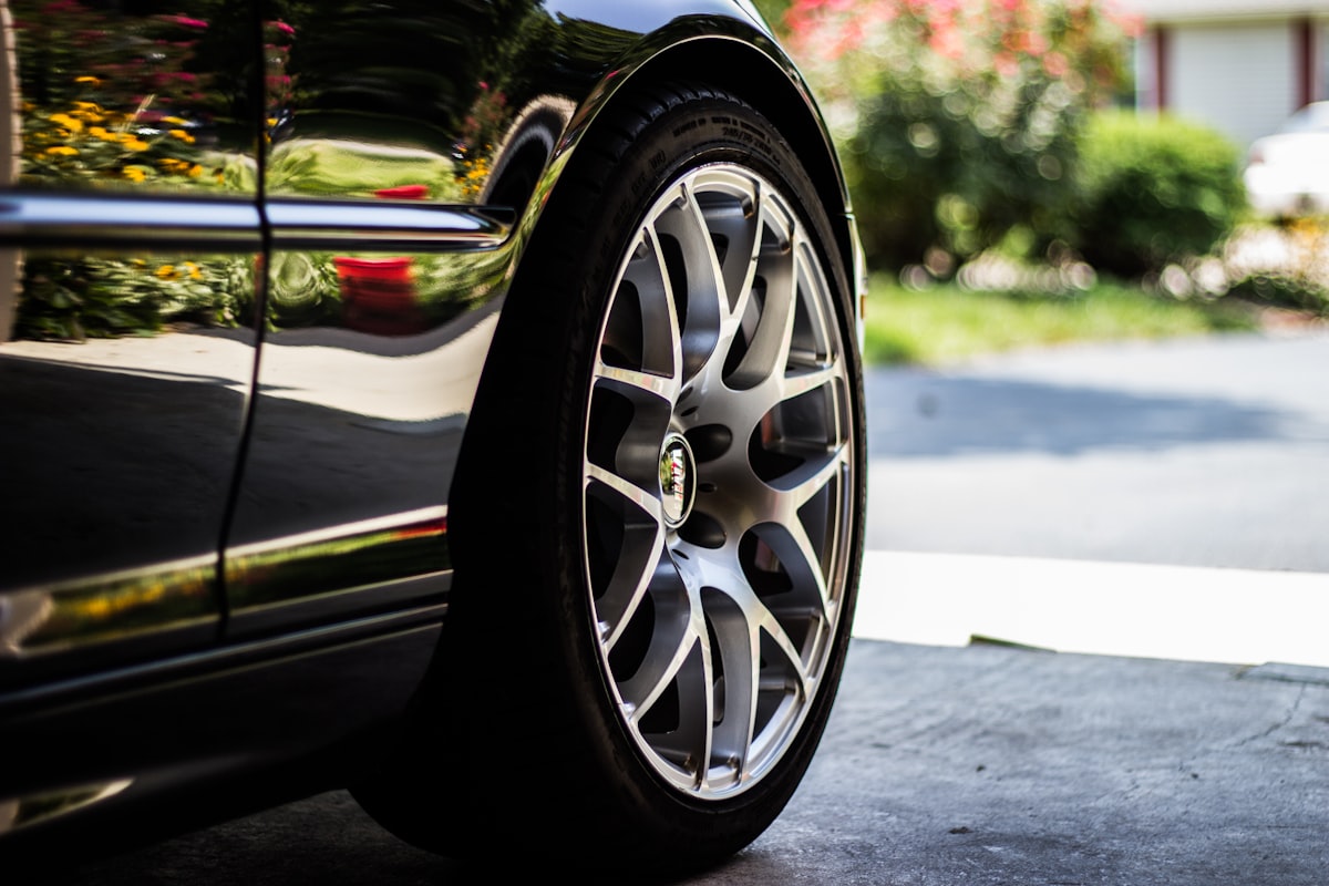 Close-up of a gray alloy wheel on a car parked in a driveway, the wheel spokes and barrel visibly coated with a fine gray film of brake dust