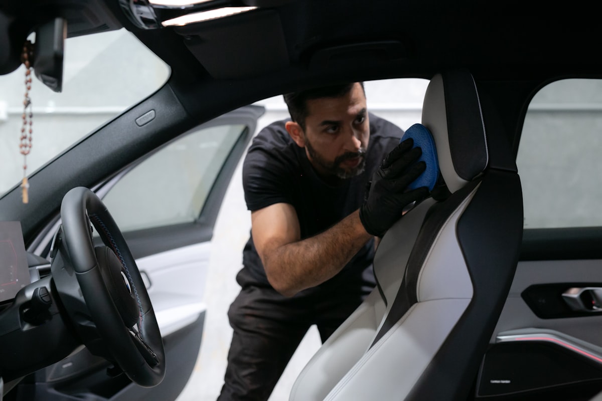 A detailer cleaning a light-coloured car seat with a microfiber cloth