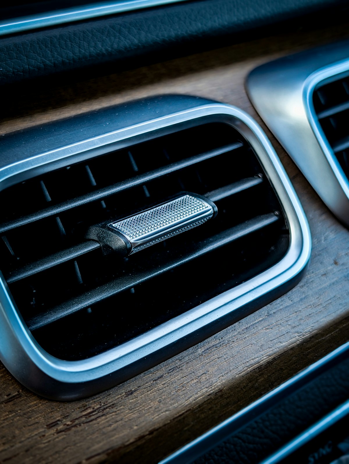 Close-up of a car's air vents on a wood-trim dashboard, where smoke odor commonly gets trapped in the ventilation system.