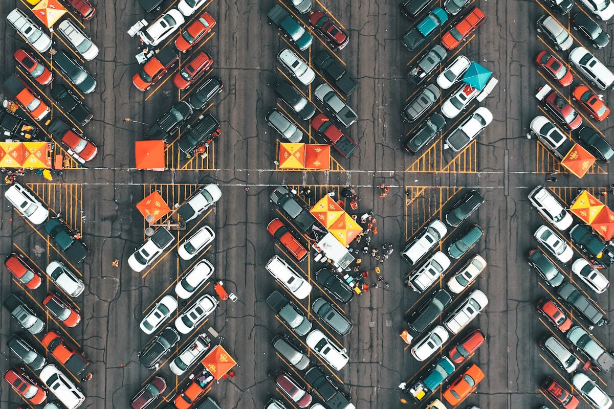 Cars parked close together in a gravel stadium tailgate lot with grills and coolers set up nearby