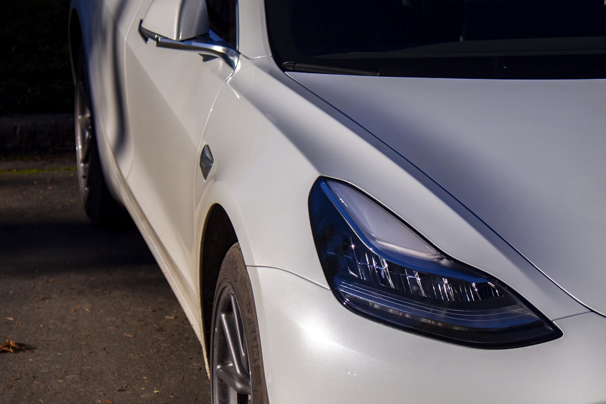 Close-up of a freshly detailed white Tesla Model 3 front fender and headlight
